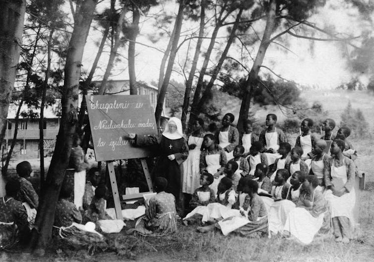 A missionary nun at blackboard gives a lesson to South African children.