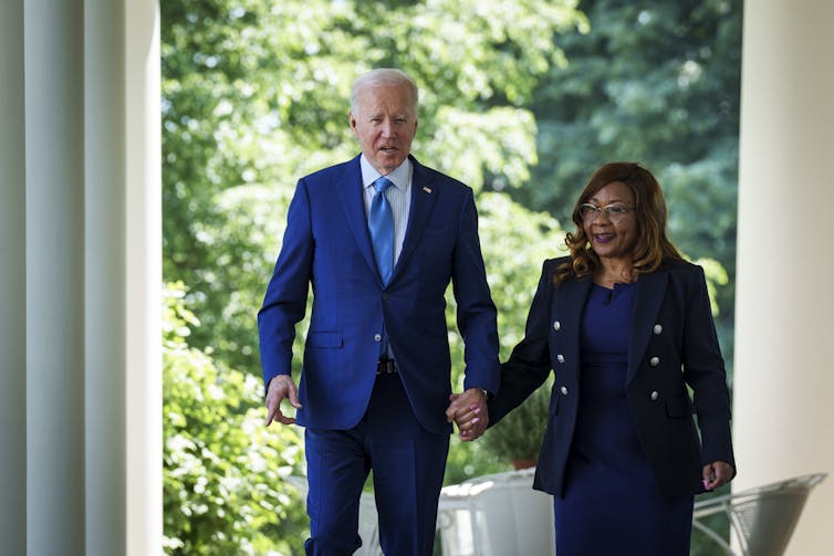 An elderly white man is holding hands and walking with a black woman.