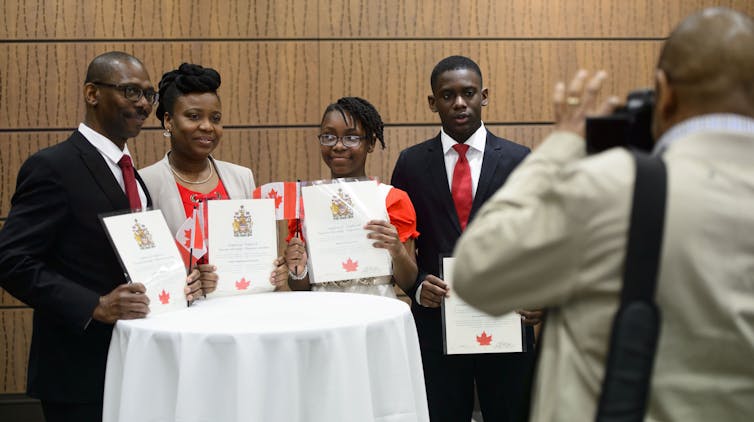A family of four holds up their citizenship certificates and smiles for a photo.