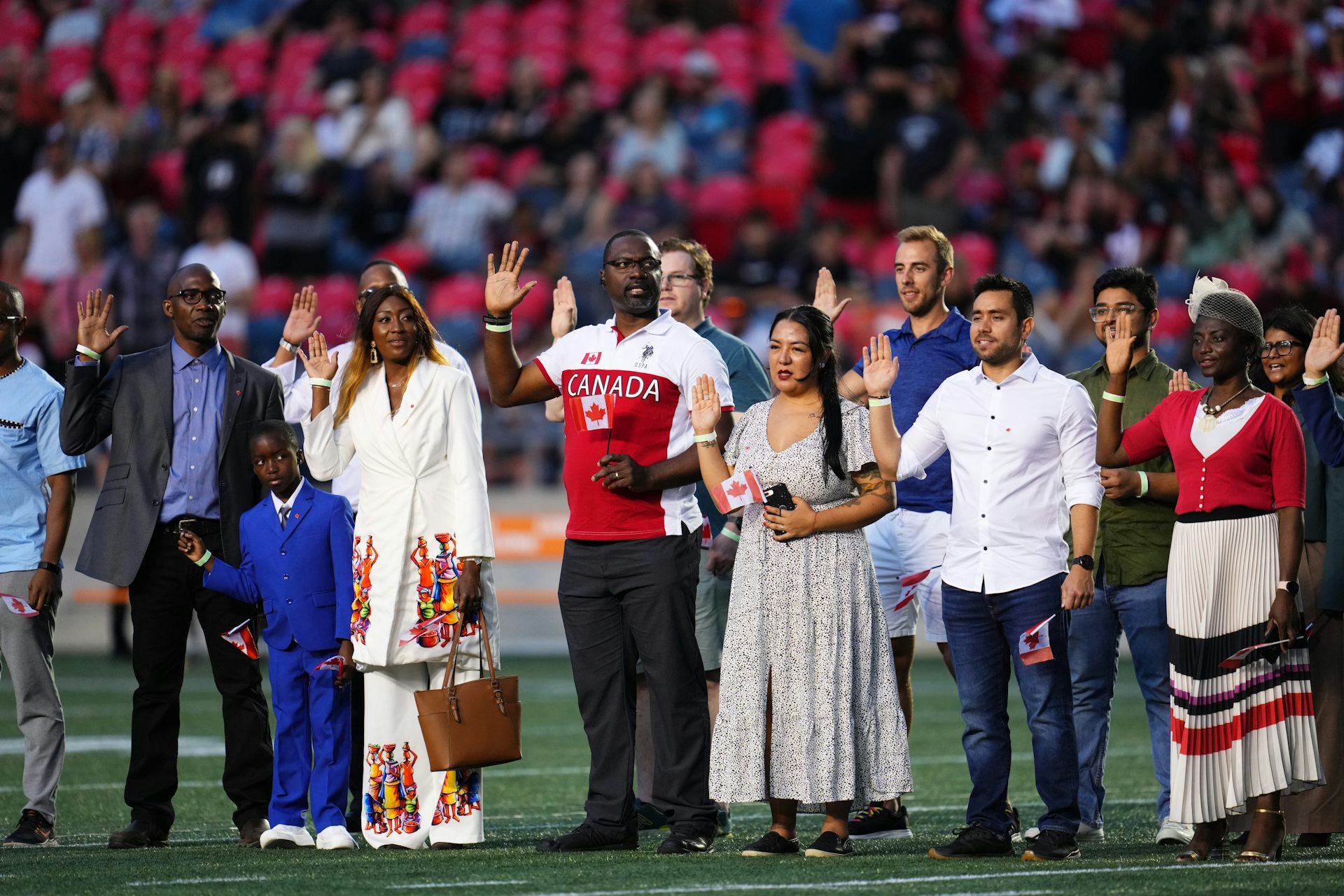 Several men and women and one boy raise their hands as they stand on a football field.