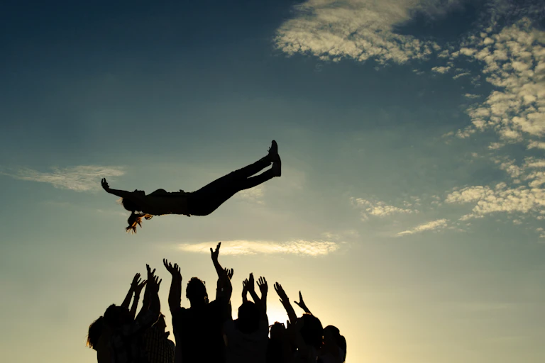 Silhouette of a group of people throwing a young woman in the air, with their arms outstretched to catch her
