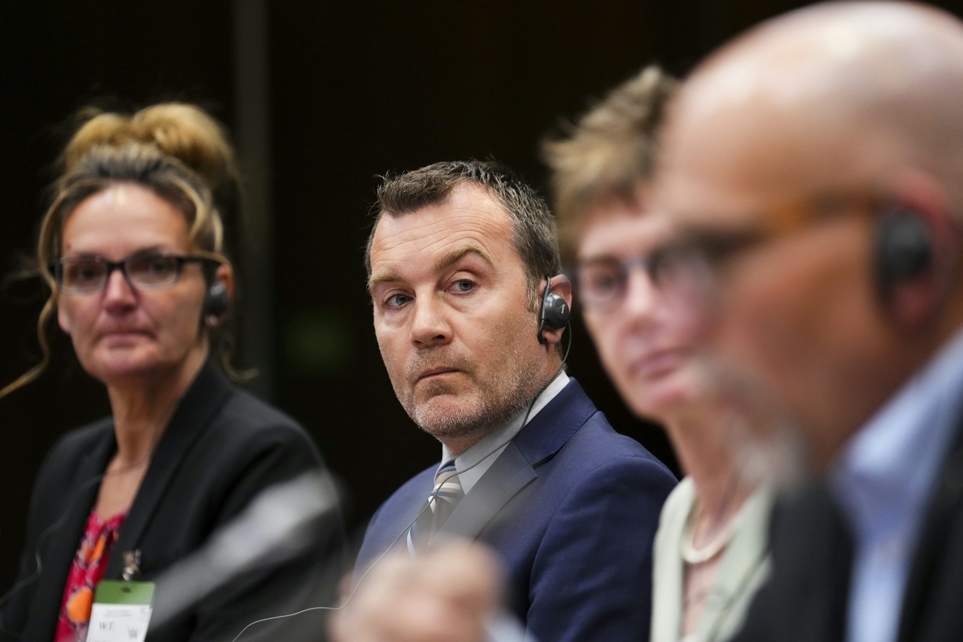 Four people sit in a row. One man speaks while the others look at him listening.