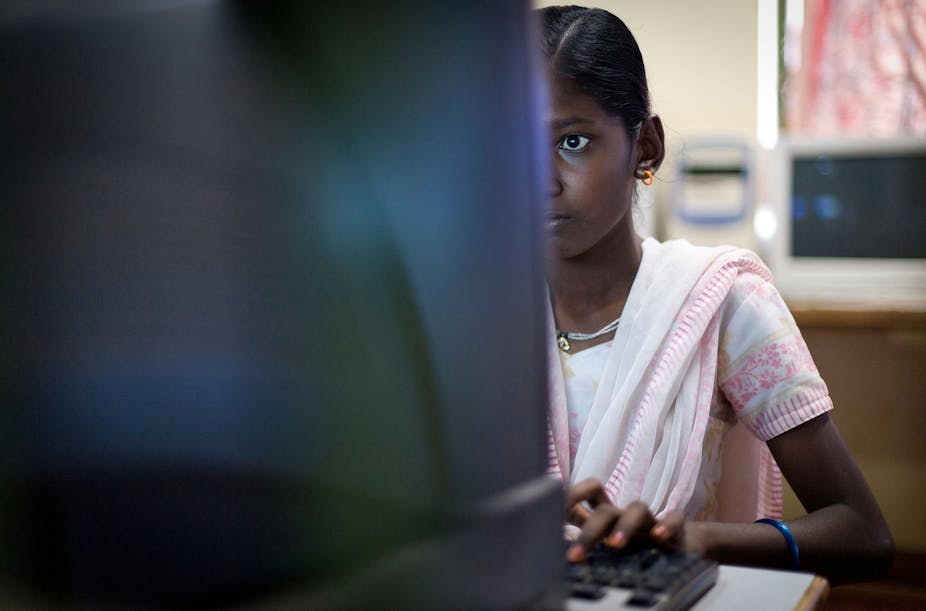 A young girl in a pale pink sari staring intently at a computer