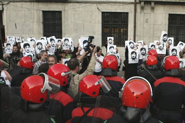 Unos manifestantes portan las fotografías de unos hombres mientras policías con cascos rojos les hacen frente.