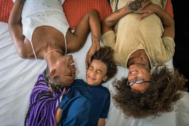 Two parents lying on bed with their child between them, smiling