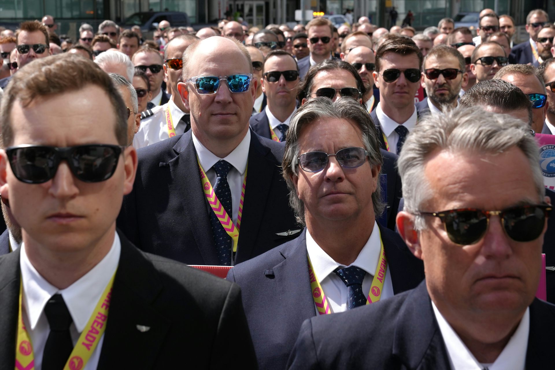 A crowd of pilots in uniform stand facing the camera. Almost all of them are wearing sunglasses.