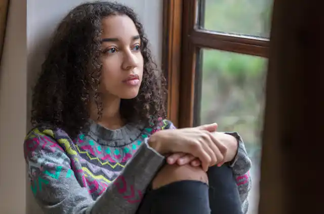 A girl sitting on a window sill looking out of the window.