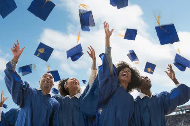 Four Black college students throw their graduation caps in the air. They are blue. So are their gowns.