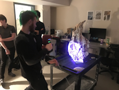 A photo of a man holding a device that illuminates a fossil with a bright purple light