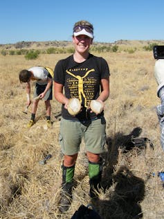 A photo of a woman standing outdoors holding two pieces of rock containing a fossil