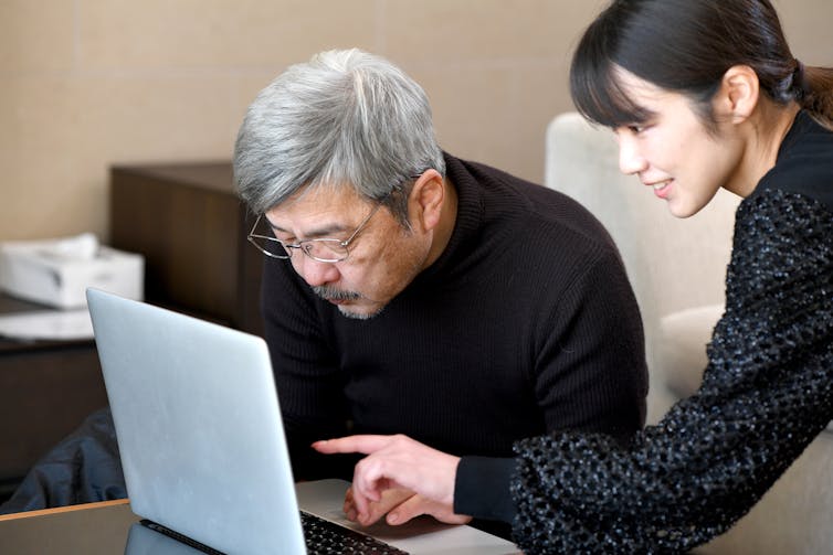 An older man looks at a computer while his daughter points to the screen.