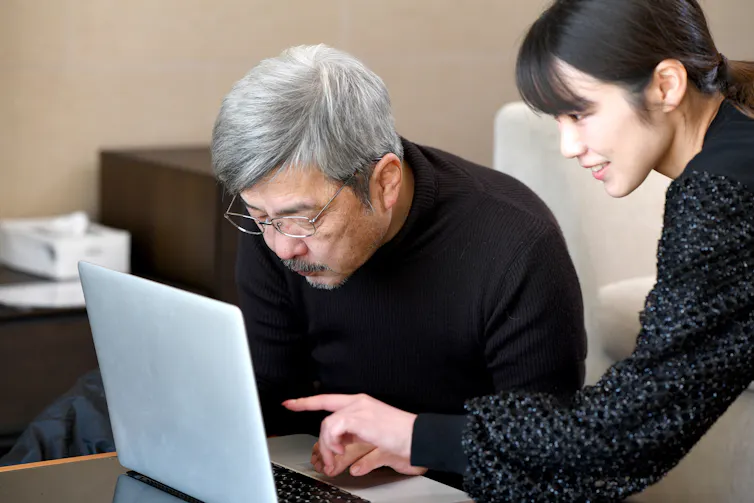 An older man looks at a computer while his daughter points to the screen.