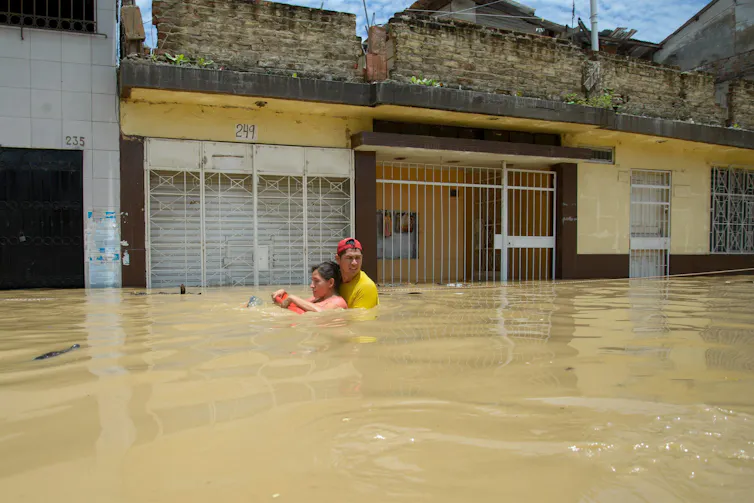 man helps woman through floodwaters