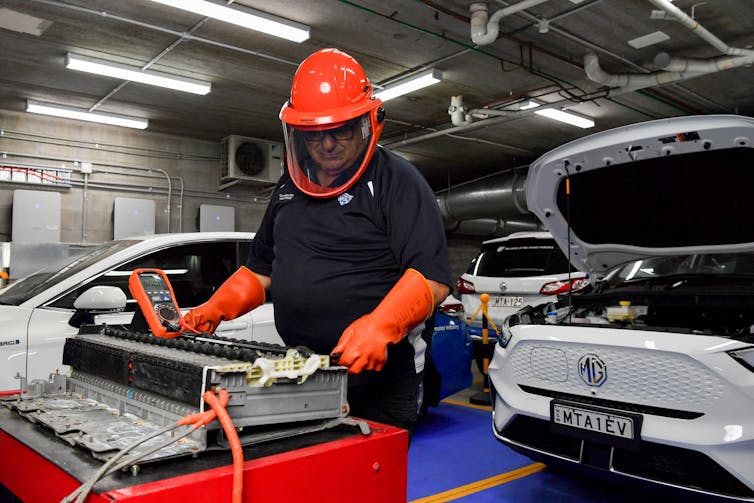 a technician works on an electric vehicle battery with cars in the background