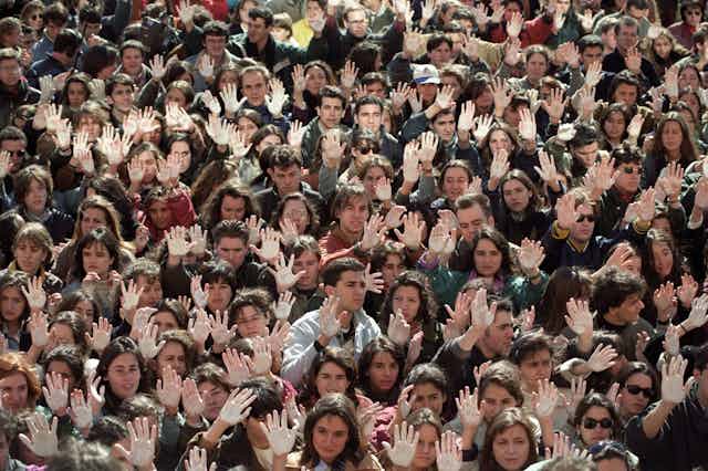 Cientos de personas alzan manos pintadas de blanco en una manifestación.