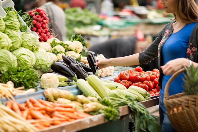 Woman choosing vegetables from a shop display.