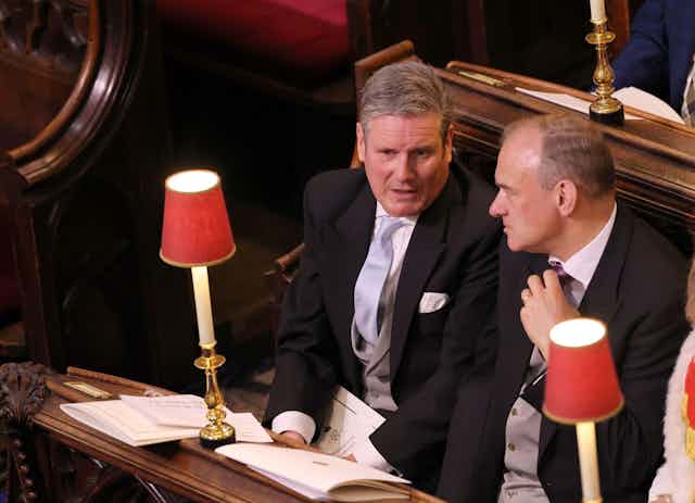 Keir Starmer and Ed Davey chatting as they sit in pews next to other guests at the coronation. 