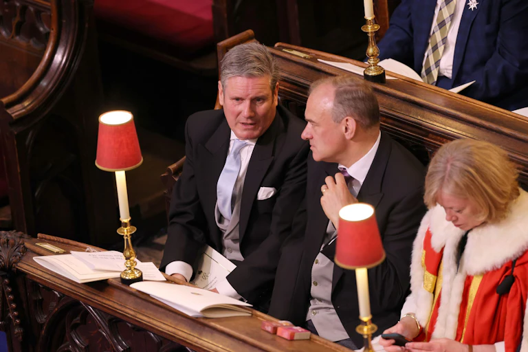 Keir Starmer and Ed Davey chatting as they sit in pews next to other guests at the coronation.