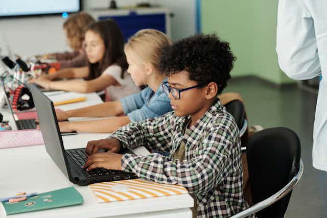 Four elementary school kids work on laptops in classroom