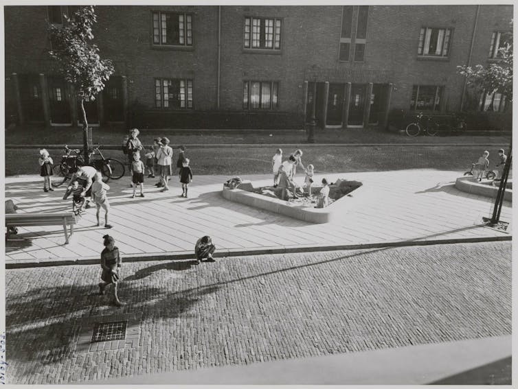An archival photograph in black and white of children playing on a playground.