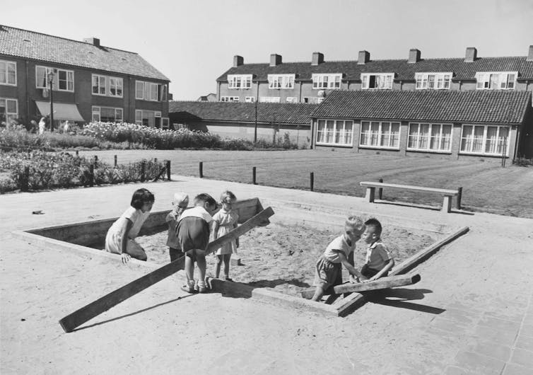 Little boys drag large timbers into a sandpit.