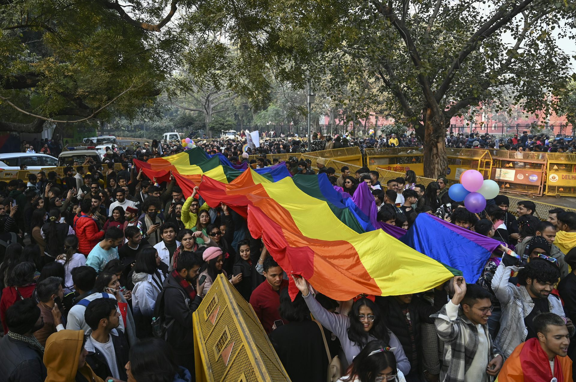 People march down a street carrying a large rainbow flag.