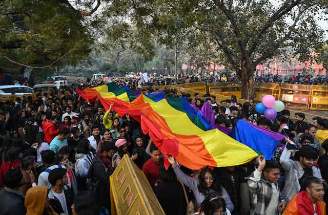 People march down a street carrying a large rainbow flag.