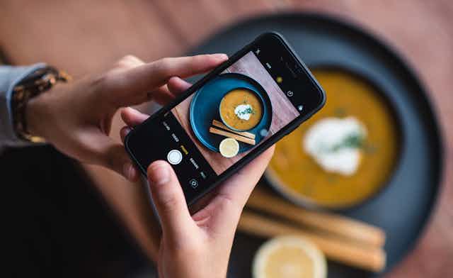 A person photographs a bowl of soup with their phone.