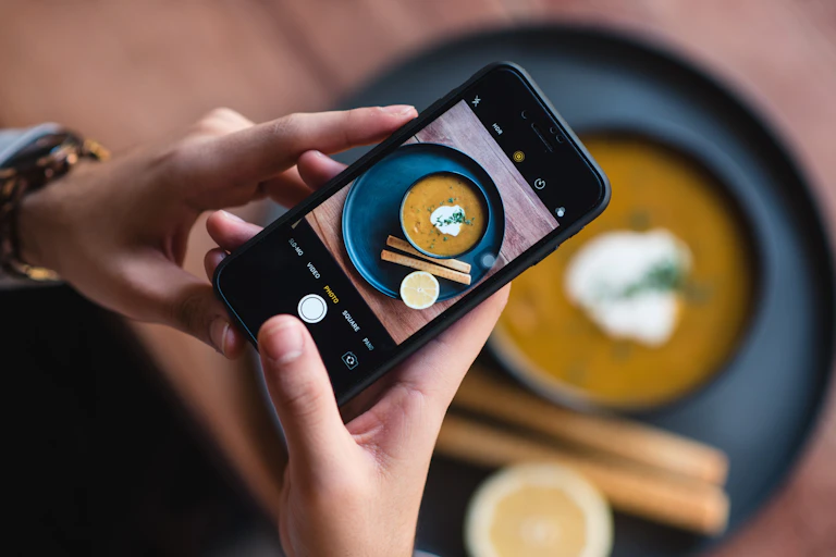 A person photographs a bowl of soup with their phone.