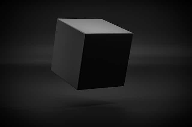 A black cube tilted at an angle hovers above a black surface