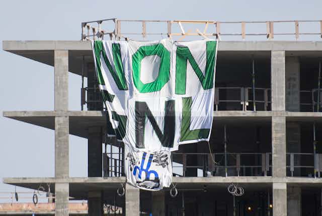 A Greenpeace banner reading ’No GNL’ is shown hanging from a building under construction.