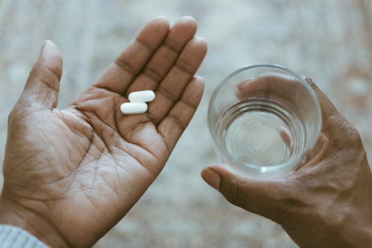 Two white pills in one hand and glass of water in the other