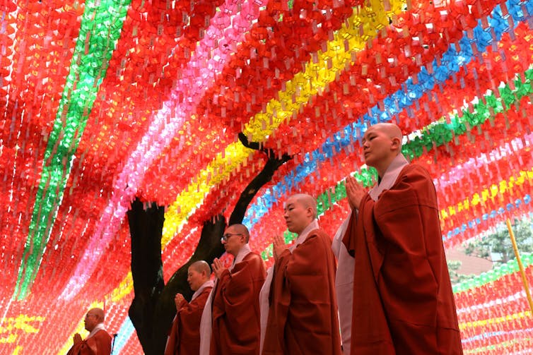 Five monks in robes stand beneath a canopy of brightly colored paper lanterns.