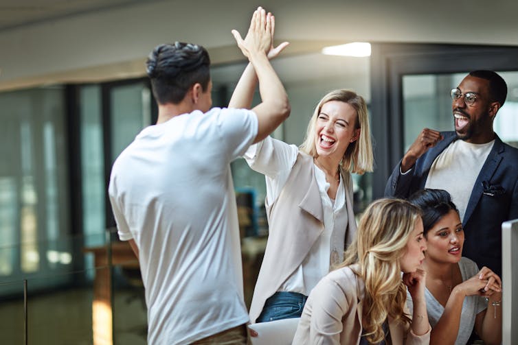 Shot of a group of colleagues giving each other a high five while using a computer together at work.