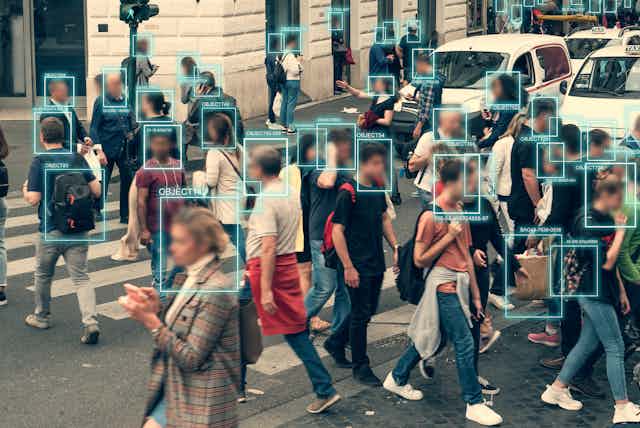 facial recognition technology being used on a crowd of people crossing the street, illustrated by blue rectangular outlines around individuals' blurred faces