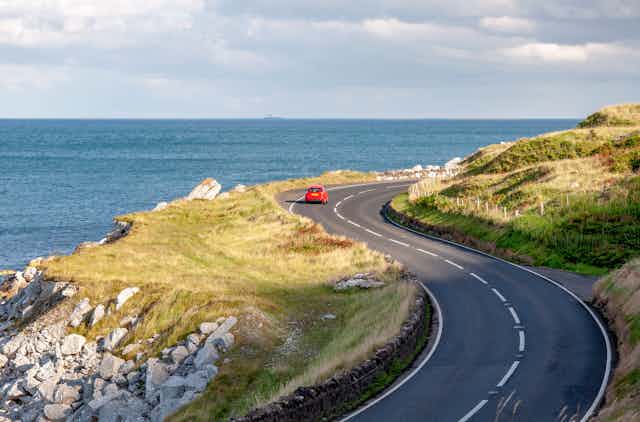A red car driving down a coastal road.