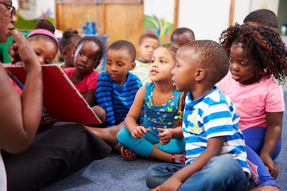 A group of young children surround an adult with a book who is reading to them