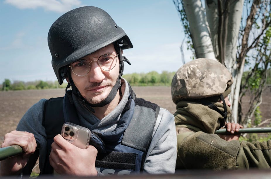 Arman Soldin, casqué et en gilet pare-balles, un smartphone à la main, aux côtés d'un militaire