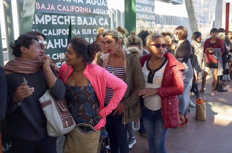 A group of people stand in a line. Some are chatting to each other.