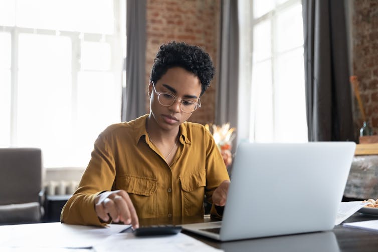 A woman at a laptop computer using a calculator.