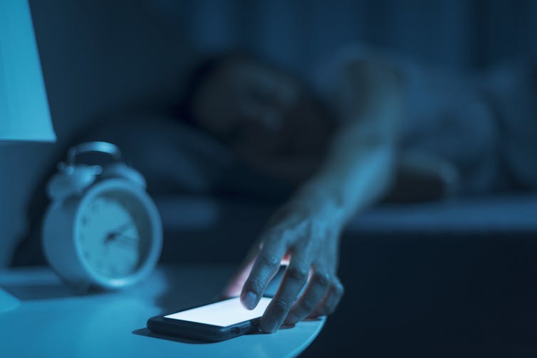Adult reaches for smart phone with lit screen on bedside table