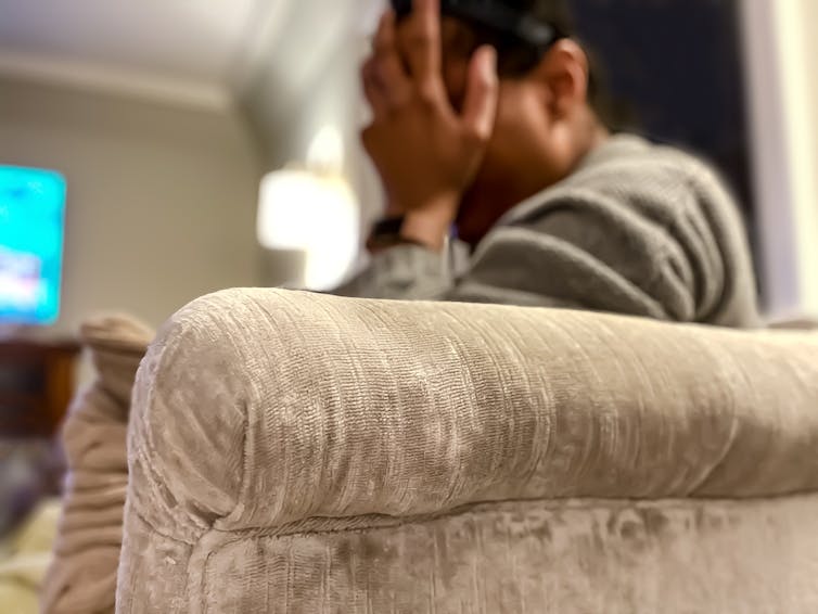 Person sitting on couch, holding head in hands.