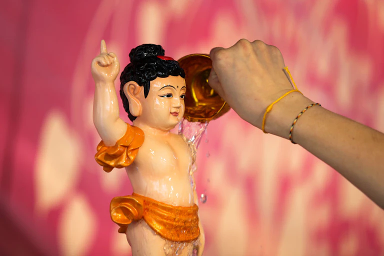 A small statue of a boy with black hair, pointing to the sky, with a person's hand pouring water over it.