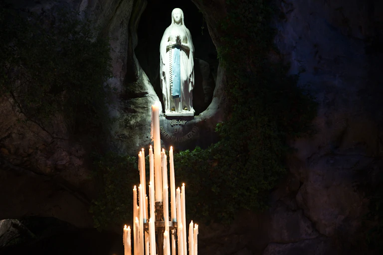 Several candles lit before Virgin Mary statue at Lourdes.