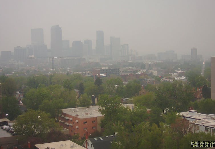 A photo looking out at the Denver skyline shows a very hazy cities
