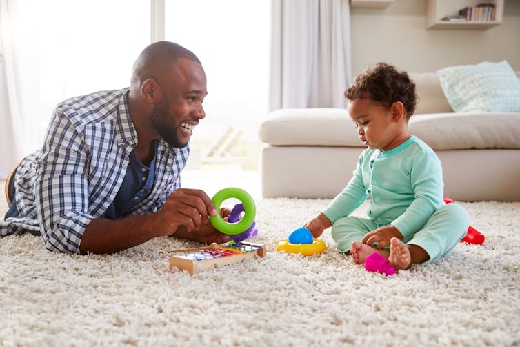 father and small child play on living room rug with coloured toys