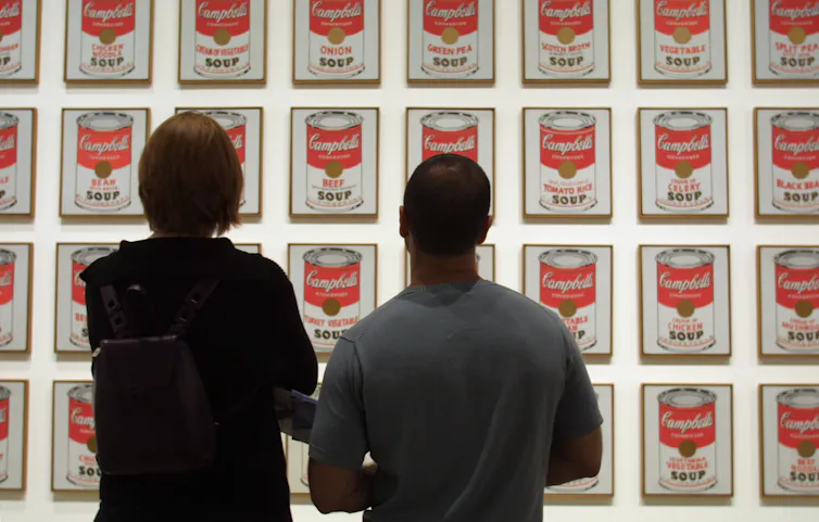 Two people in a gallery look at Warhol's soup cans