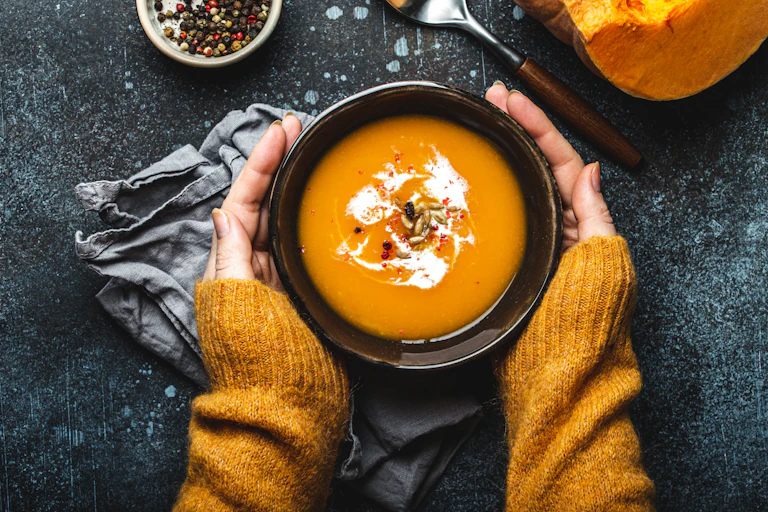 Hands holding a bowl of pumpkin soup