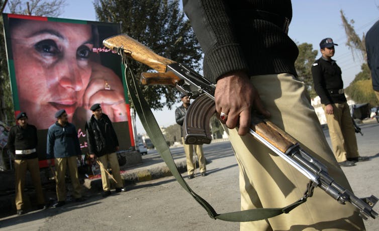 picture of armed security personnel next to a poster of a Benazir Bhutto