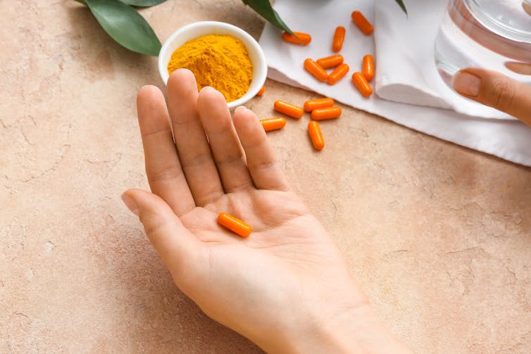 A person holds a turmeric supplement in the palm of their hand.